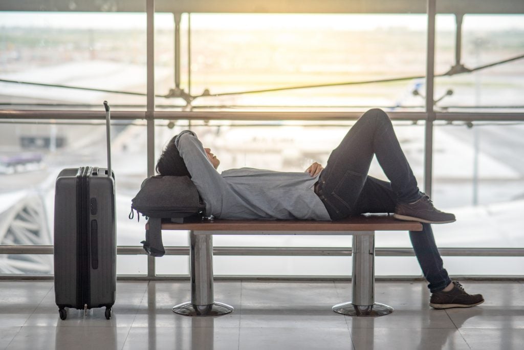 Hombre tapandose la cara acostado en el aeropuerto